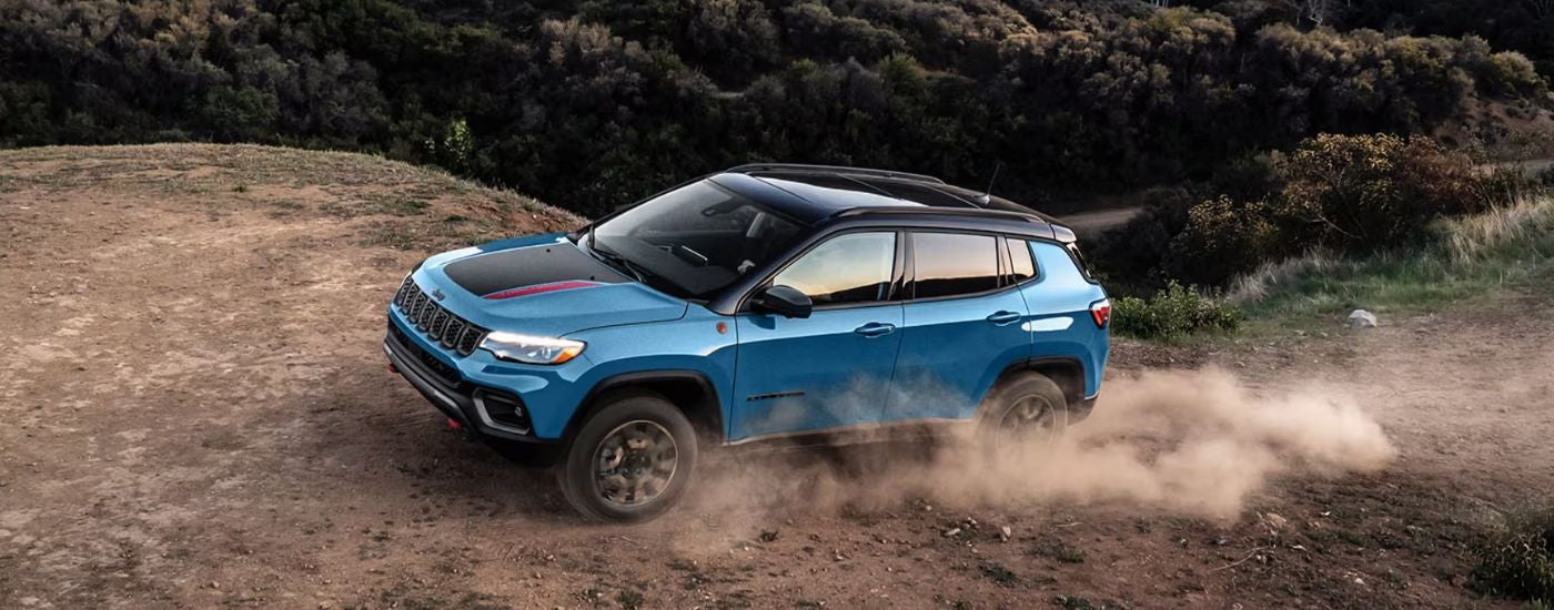 Blue 2026 Jeep Compass Trailhawk driving on an off-road trail.
