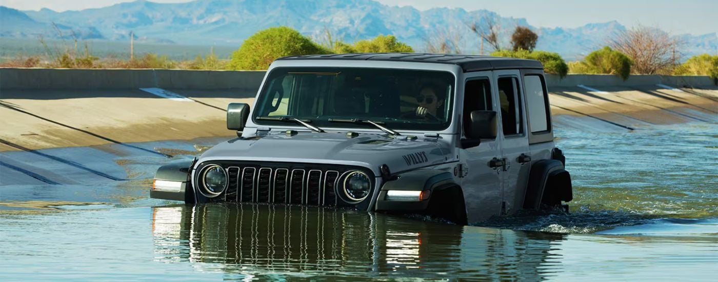 Grey 2026 Jeep Wrangler driving while partially submerged in water.