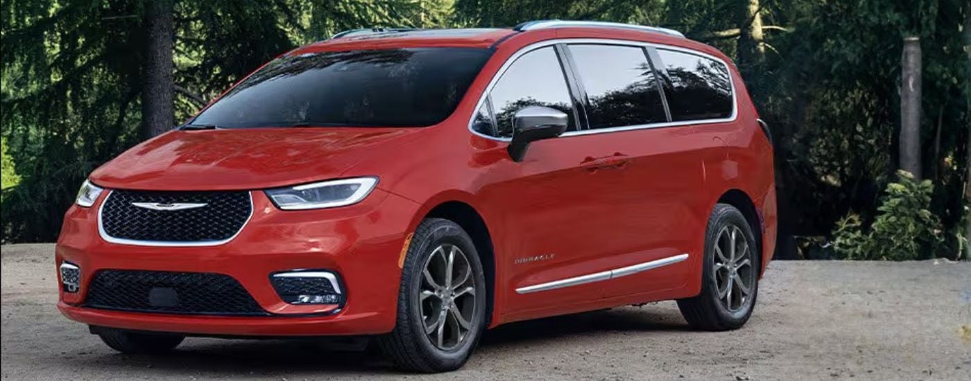 Red 2026 Chrysler Pacifica parked in front of trees.