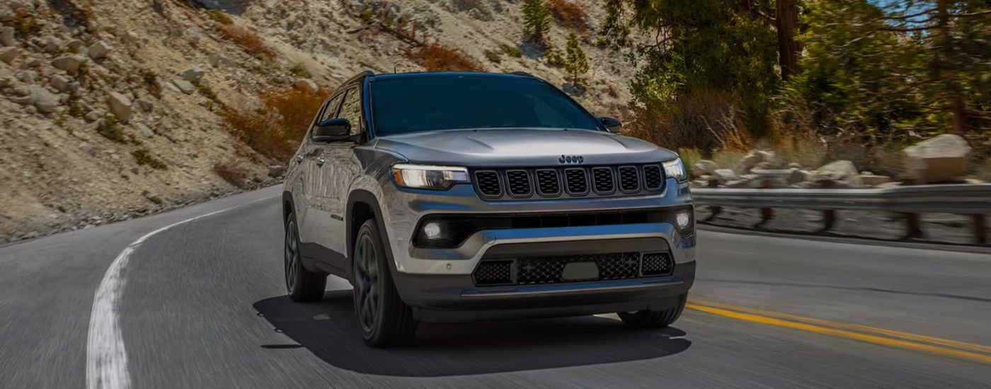 Silver 2026 Jeep Compass Limited Altitude driving on the highway in the mountains.