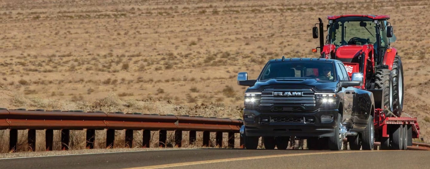 A black 2026 Ram 3500 towing a tractor.