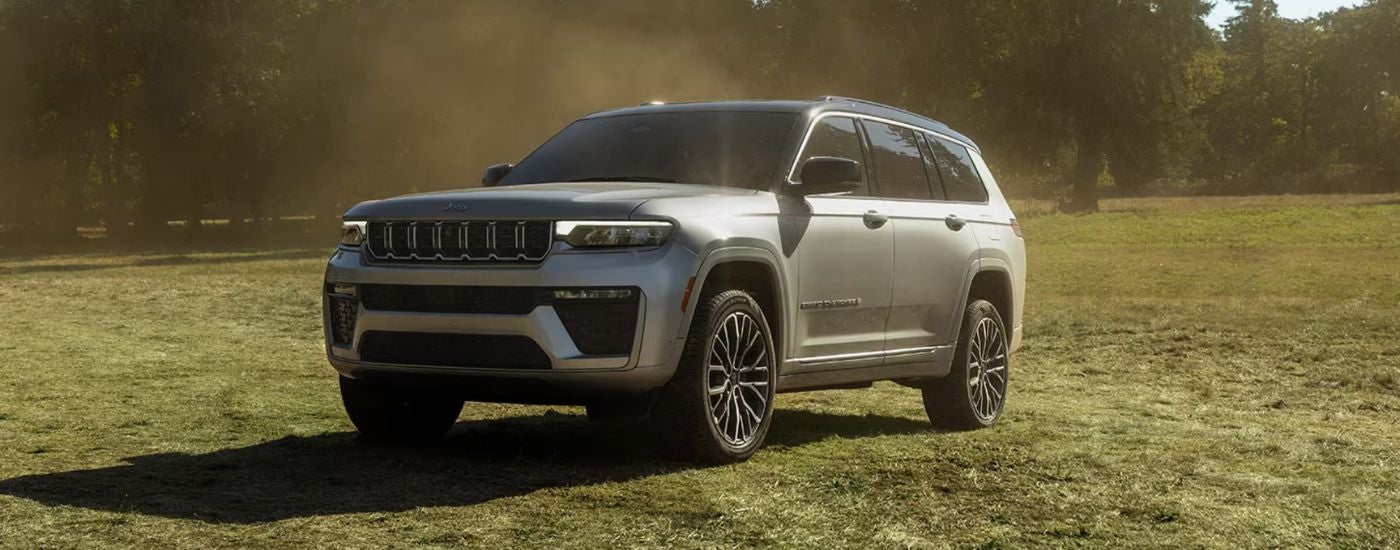 A silver 2026 Jeep Grand Cherokee parked at an angle on a grassy field.